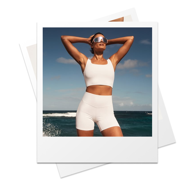 Donna in top e shorts chiari con le braccia dietro la testa davanti al mare, stampa polaroid